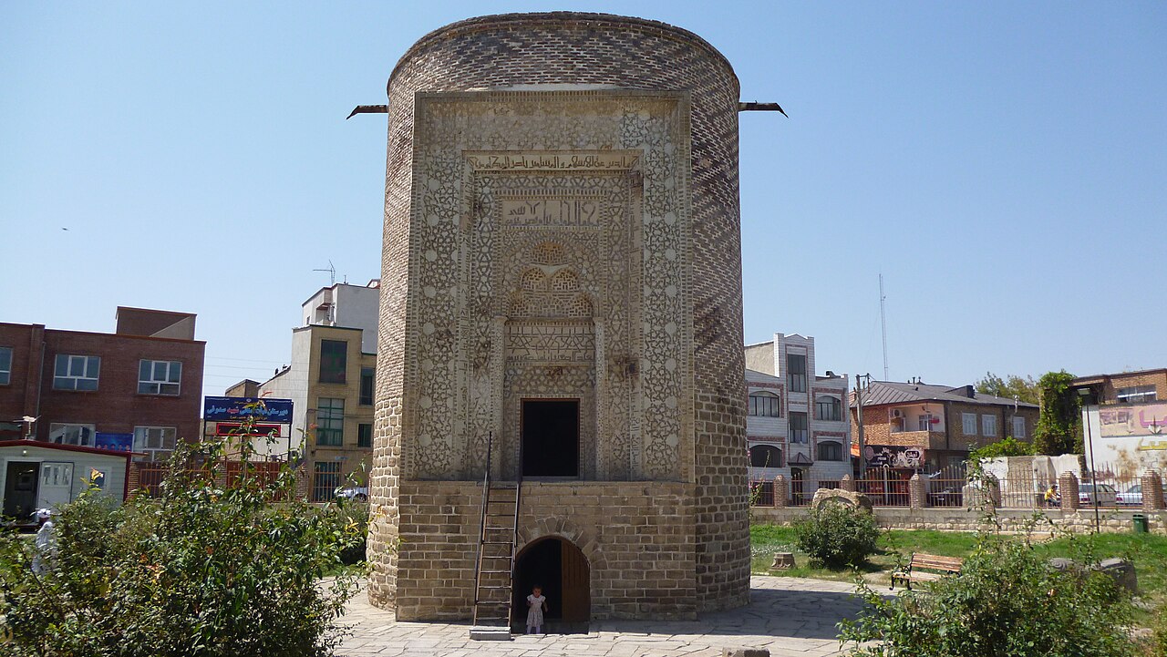 Urmiye'deki Üç Günbed Türbesinin giriş cephesi: tuğla silindirik kule, süslemeli taçkapı ve kitabe kuşağı